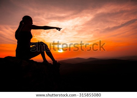 Silhouette of woman sitting on rock during the sunset meditation and pointing