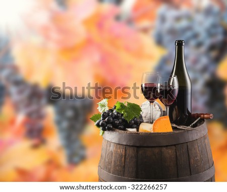 Red wine bottle and glass on wooden keg. WIne grapes on background