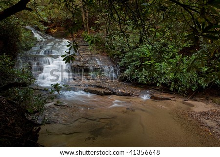 Waterfall, blurred by slow exposure, falls into stream in forest.