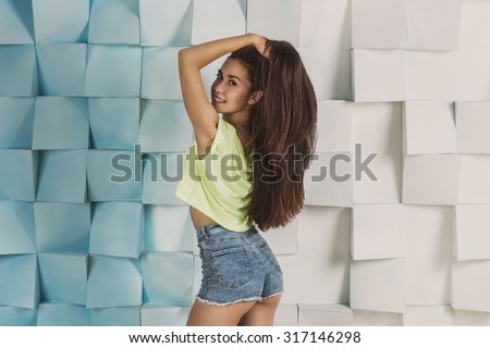 Young beautiful smiling fit girl with long dark thick hair wearing high waistline jeans shorts and bright colored t-shirt