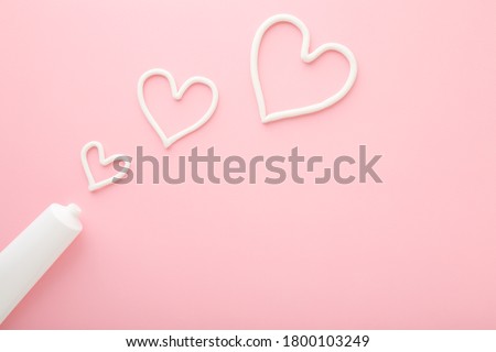 Heart shapes created from cream. White tube on light pink table background. Pastel color. Care about face, hands, legs and body skin. Closeup. Empty place for text or logo. Сток-фото © 