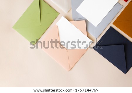 Close-up colorful mail envelopes on beige background flat lay with copy space, top view. Mailing concept isometric. White paper blank mockup for letters, greeting card, postcard, invitation
