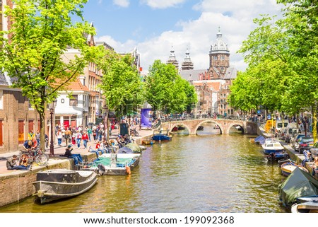 AMSTERDAM, NETHERLANDS - MAY 31, 2014: Tourists walking by a canal in Amsterdam. Amsterdam is the capital of the Netherlands and the canals and harbours fill a full quarter of the city surface.