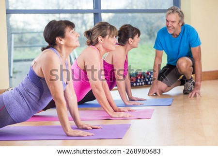 Three women using gym equipment to do stretches with a senior man encouraging them