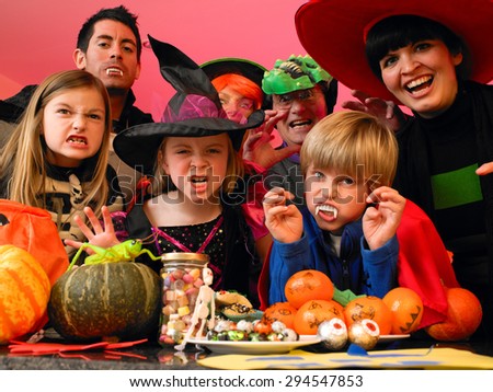 Family/friends posing for the camera in their halloween costumes. They are standing in the kitchen with party food and treats set out in front of them.