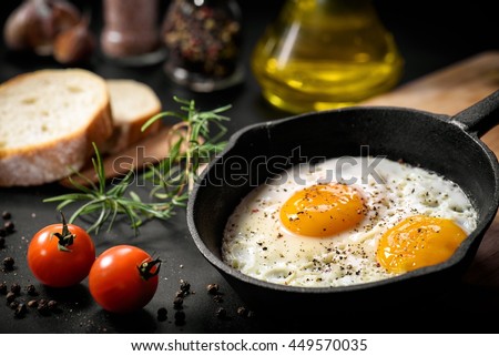 Fried eggs in a frying pan with cherry tomatoes and bread for breakfast on a black background. 商業照片 © 
