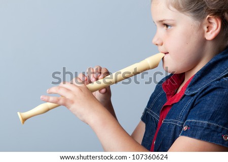 Little girl plays the flute on a grey background