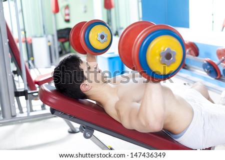 Strong handsome man lifting heavy free weights at the gym