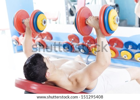 Shirtless young man lifting heavy free weights at the gym