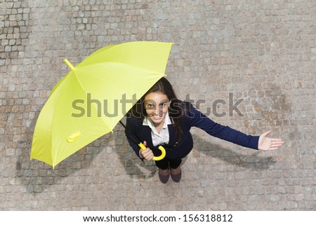 Smiling young business woman with yellow umbrella checking if it\'s raining