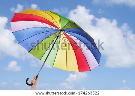Rainbow umbrella in woman hands against cloudy sky