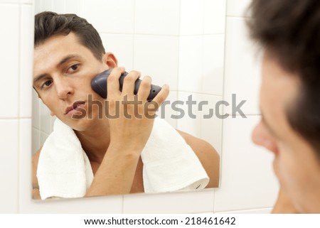 Young man shaving with electric shaver at the bathroom