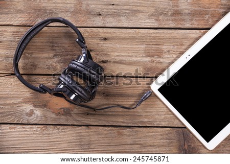 Tablet computer with headphones against wooden background
