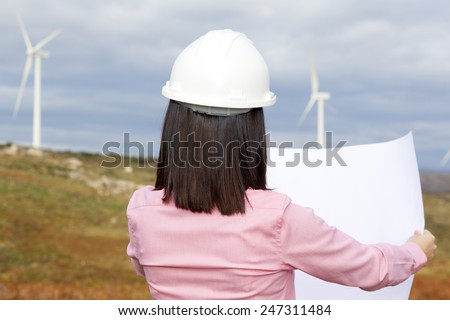 Back view of female engineer holding a blueprint at wind turbine site