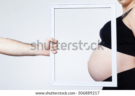 Man hand framing the belly of a pregnant woman on grey background