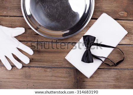 Top view of a waiter tray, bow tie, gloves and a napkin on wooden background