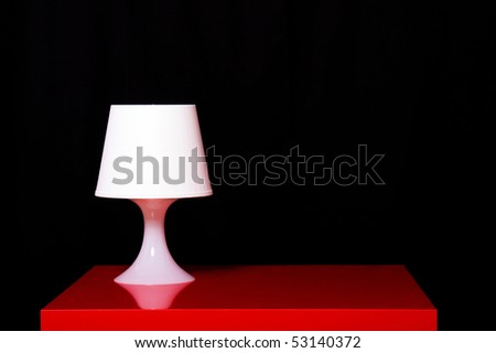 White modern lamp on a red table against dark background