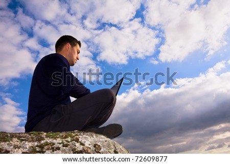 Young man sitting on the top of mountain working with laptop