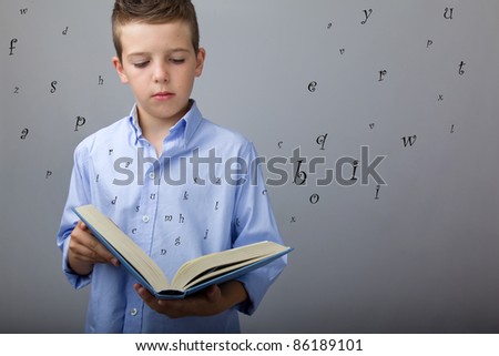 cute boy reading a book with flying letters, studio shot