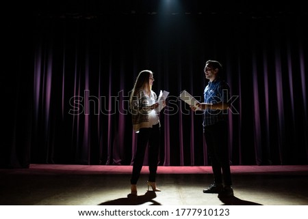 Rehearsal at theatre. Man explain to student actress how to play on the stage on the new performance for public. Dark hall at background.