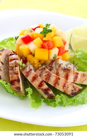 Grilled chicken breast with fresh mango salsa on white plate
