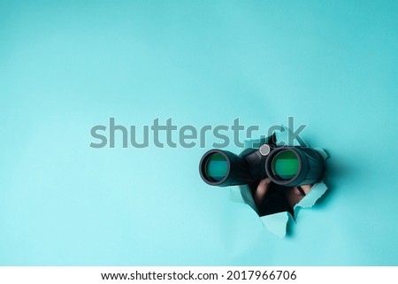 Female hand holds black binoculars on a blue background. Journey, find and search concept. Banner.