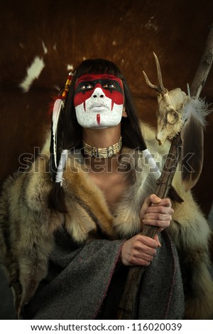 Native american woman portrait with painted face. Young beautiful woman in native american costume with wolf fur and war mask on her face holding a medecine staff