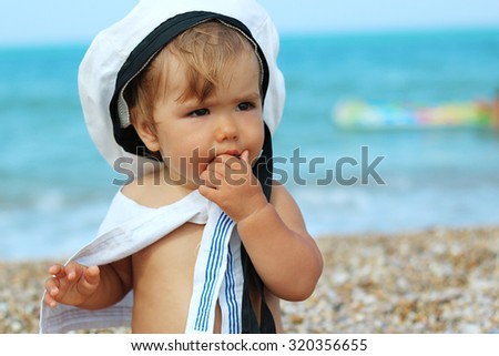 Playful baby girl sitting in sailor clothes on sea background, outdoor