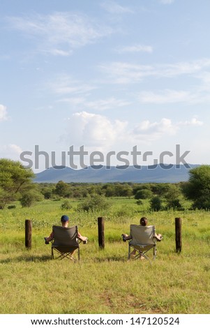 A caucasian couple sitting on two camping chairs looking out over the green savanna of Africa