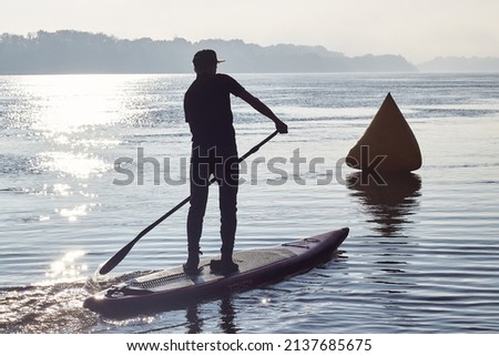 Silhouette of teenager rowing on SUP (stand up paddle board) at sunrise in a haze at Danube river Stock fotó © 