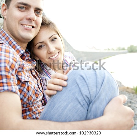 love guy with the girl in striped shirts and blue jeans sitting on the stone waterfront on the stage with a fixed metal wire