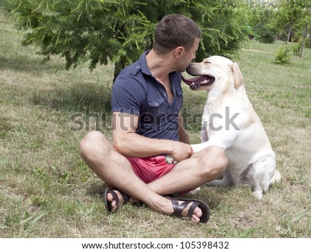 adult man sitting on the lawn and keeps your pet\'s paw in - dog - Labrador