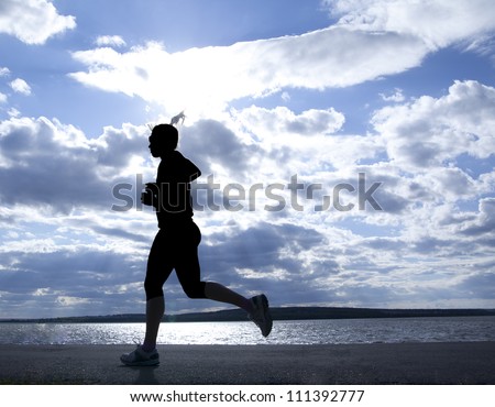 Female runner full length silhouette against the blue sky and sun