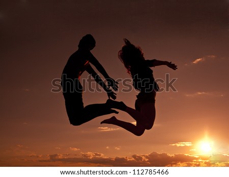 Silhouettes of couple jumping on orange sunset background