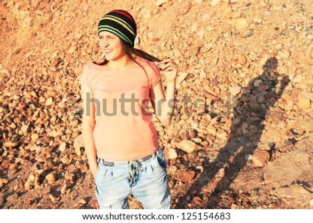 Portrait of young woman in pink shirt and rastaman cap looking to the left on red mountain background