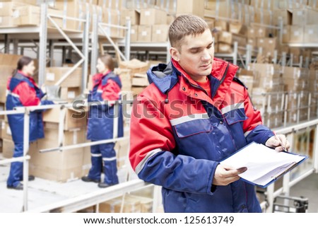 warehouse three workers - one man and two woman in a special uniform is recording and accounting of the contents in cardboard boxes in stock