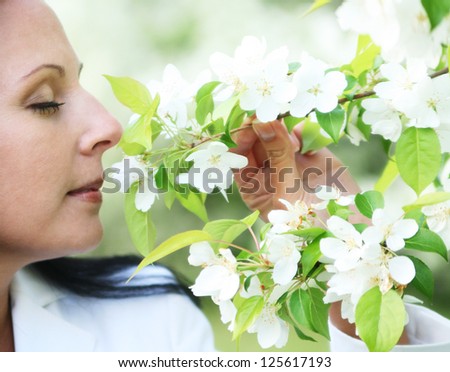 beautiful young brunette curly woman standing near the apple tree and breathes the fresh scent of flowering