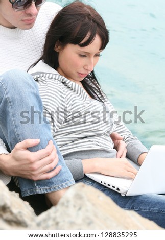 Happy young couple sitting together near the sea with a laptop.