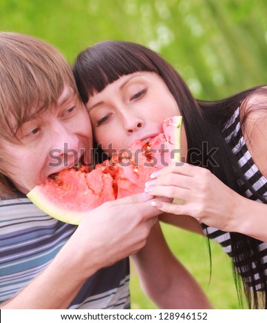 Young couple eating water melon. Pair with a watermelon couple on a picnic in the forest together bite a one piece of watermelon - a symbol of unity and oneness