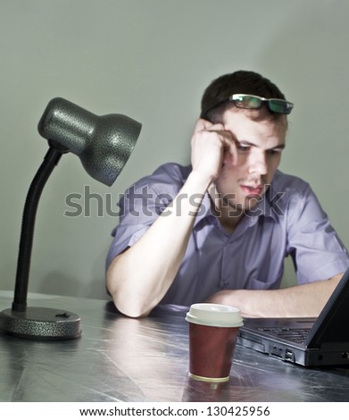 man in evening light, table lamp talking on a cell at his desk in front of a black laptop