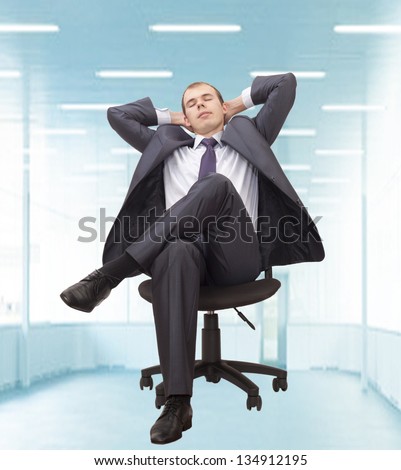 Relaxed businessman with hands behind his head in a large empty office in the blue light of day