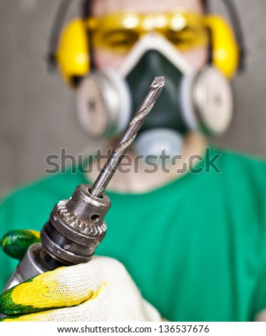 Worker with a drill in yellow protective glasses, ear plugs and respirator    focus on the drill drills