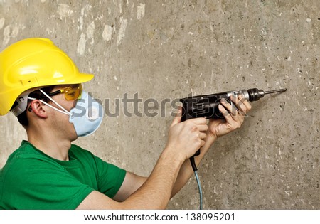 Worker with a drill in yellow protective glasses, ear plugs and respirator focus on the drill drills