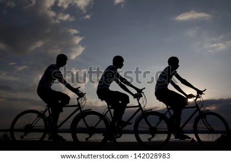 Image of sporty company friends on bicycles outdoors against sunset. Silhouette The three phases of motion of a single cyclist along the shoreline coast