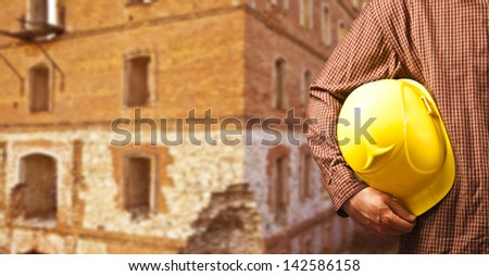 working hands without gloves holding a yellow hard hat close-up on the red bricks wall background
