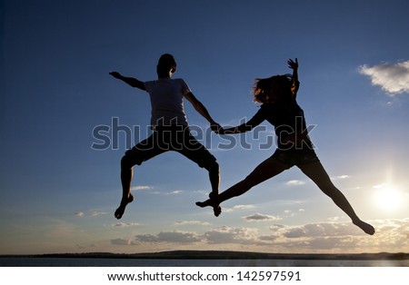 Silhouettes of couple jumping on blue sunset background