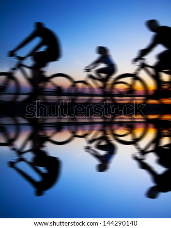 Image of sporty company friends on bicycles outdoors against sunset Silhouette with reflection on water . A lot phases of motion of a single cyclist along the shoreline coast Space for inscription