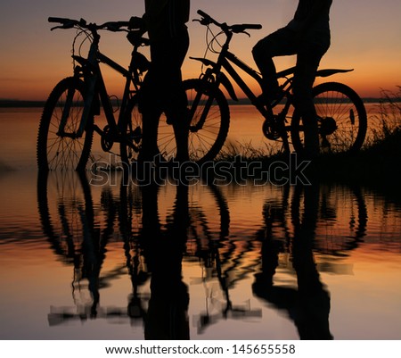 silhouettes of couples in love ride bicycles along the beach with reflection on water No faces
