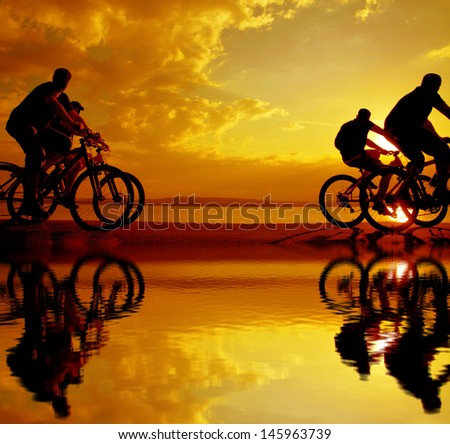 Image of sporty company friends on bicycles outdoors against sunset. Silhouette A lot phases of motion of a single cyclist along shoreline coast Reflection on water copy Space between for inscription