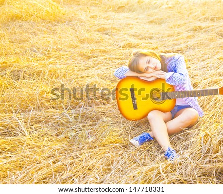 Country girl sitting with guitar at wheat field  Copy space for inscription